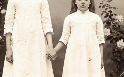 ” This 1895 Photo of a Girl Holding Her Sister’s Hand Seemed Normal — Until Restoration Revealed………” When museum curator Dr. Helen Foster examined this 1895 photograph in 2021, she saw what everyone else had seen for 126 years. Two sisters in matching white dresses holding hands in a garden, their faces serious in that typical Victorian way. The photograph had been donated anonymously to the Boston Historical Society with only a handwritten note. The Davy’s sisters, 1895. May they finally rest. Helen almost filed it away without a second thought. But then she noticed something odd about the smaller girl’s hand. The way the fingers curled, the unnatural angle. She ordered a highresolution scan. What the restoration revealed made Helen understand why this photograph had been hidden for over a century and why the note said, “Finally, rest. This isn’t just a photograph of two sisters. It’s a photograph of a promise that lasted beyond death. The photograph arrived at the Boston Historical Society on March 15th, 2021 in a plain manila envelope with no return address. Inside was a single sepia toned photograph approximately 5×7 in mounted on thick cardboard backing typical of 1890s studio photography. The image showed two girls standing in what appeared to be a garden. The older girl, perhaps 10 or 11 years old, stood on the left wearing a white Victorian dress with lace collar and puffed sleeves. Her dark hair was pulled back severely from her face. Her expression was solemn, almost haunted. Beside her stood a smaller girl, maybe six or seven, also in white. She was shorter, thinner, with the same dark hair and serious expression. The younger girl’s right hand was held by the older girl’s left hand. Their fingers were intertwined tightly. Behind them was a backdrop of climbing roses on a trellis. Soft afternoon light suggested the photograph had been taken outdoors, which was unusual for the era when most portraits were done in studios with controlled lighting. At the bottom of the photograph, written in faded brown ink, were the words, “Liy and Rose Davies, June 1895. ” The accompanying note written on modern paper in shaky elderly handwriting, said only, “The Davy’s sisters, 1,895. May they finally rest. I can’t keep this any longer. Someone should know the truth. Dr. Helen Foster, age 52, had been curator of the photographic archives at the Boston Historical Society for 18 years. She had seen thousands of Victorian photographs. This one seemed unremarkable at first glance, just another formal portrait of children from a wealthy family, the kind of image that filled countless archives across the country. But something bothered Helen. She couldn’t quite identify what it was. She examined the photograph more closely with a magnifying glass. The older girl, Lily, according to the inscription, had her eyes focused directly on the camera. Her expression was difficult to read, not quite sad, not quite angry, something closer to resignation or perhaps determination. The younger girl, Rose, had her head tilted slightly toward her sister. Her eyes were also on the camera, but they seemed unfocused, glazed. Her mouth was slightly open, and then Helen noticed the hand. Rose’s hand, the one holding Lily’s, had an odd quality to it. The fingers were curled in a way that didn’t seem natural. The skin tone appeared slightly different from the rest of her visible skin. darker perhaps or discolored in a way that the sepia tone didn’t quite hide. Helen pulled out her measurement tools and examined the photographs dimensions and mounting style. Everything was consistent with 1895 photography techniques. The image wasn’t a modern forgery, but there was something wrong about it that she couldn’t articulate. She decided to have the photograph digitally scanned at the highest possible resolution. The society had recently acquired a new scanner capable of capturing detail at 12,800 dpi, resolution that would reveal things invisible to the naked eye, things that Victorian photographers and viewers would never have seen. The scan was scheduled for March 18th, 3 days later. Helen placed the photograph in an archival storage box and tried to put it out of her mind…………..Full story below 👇👇👇